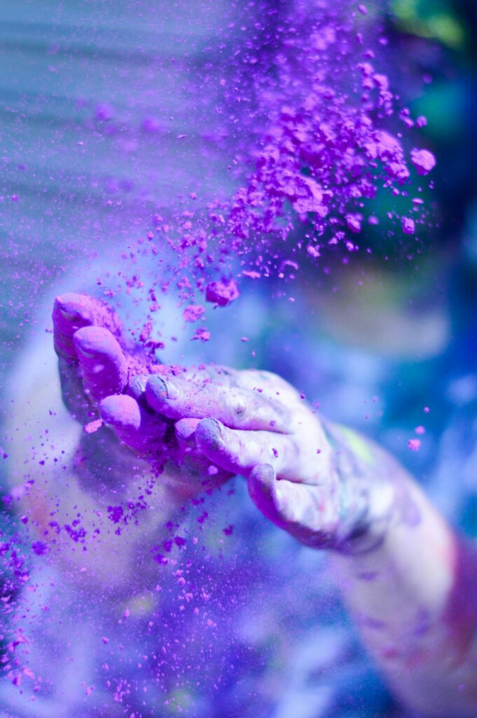 pexels-photo-1927595-1927595 Close-up of hands throwing vibrant purple powder outdoors, capturing motion and color.